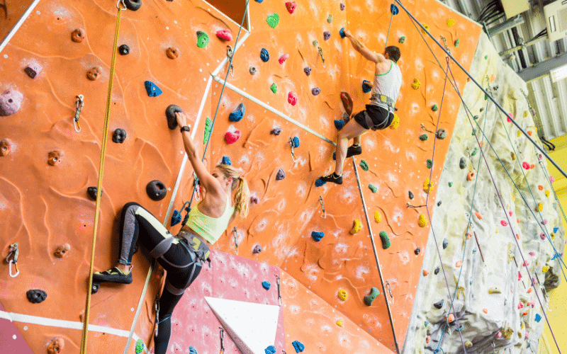 A group of young climbers are participating in a training course, learning and practicing various climbing techniques on a colorful indoor climbing wall