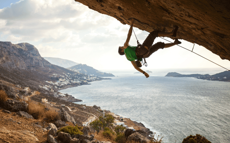 A climber ascends a challenging route, surrounded by cheering spectators and judges. The tension in the air is palpable as the climber reaches for the next hold, pushing their limits in the competitive atmosphere